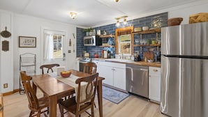 A kitchen with a wooden table, chairs, a stainless steel refrigerator, and a blue tiled backsplash.