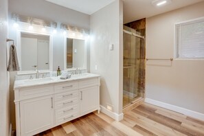 Un baño con un tocador espacioso, cabina de ducha de vidrio y ventana con persianas.