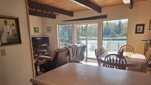 Une cuisine dotée d’un grand îlot central, d’un coin repas avec des chaises en bois et d’une vue sur un lac, visible à travers des portes vitrées.