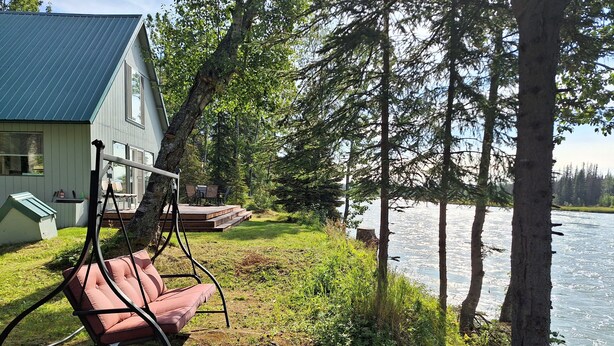 Un chalet au bord du lac, doté d’une chaise suspendue, d’une terrasse et offrant une vue sur l’eau.