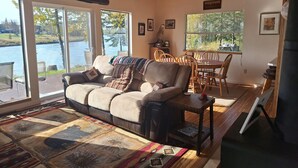 Un salon confortable avec un canapé, une table à manger et des chaises. De grandes fenêtres offrent une vue sur un lac.