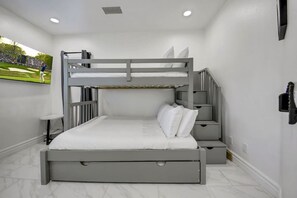 Una cama litera con escritorio y silla, una mesita pequeña y un teléfono en la pared.