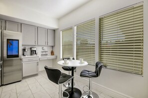 A modern kitchen with a built-in refrigerator, a coffee maker, and a digital clock. There are two black chairs around a small white table. - Desert Pearl: Pool, Spa, Pool Table, Foosball, EV! (Indio)