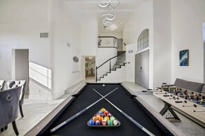 Una mesa de billar junto a una mesa de futbolín, y una escalera que sube a un nivel superior.