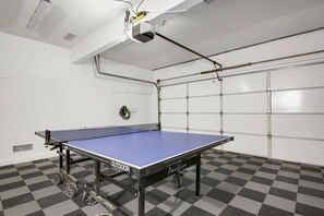 Una mesa de ping pong con ruedas, un proyector montado en el techo y una puerta de garaje al fondo.