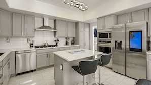 A modern kitchen with stainless steel appliances, a central island with bar stools, and a built-in microwave. - Desert Pearl: Pool, Spa, Pool Table, Foosball, EV! (Indio)
