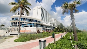 A modern hotel with a curved facade, palm trees, and a pathway leading to the entrance.