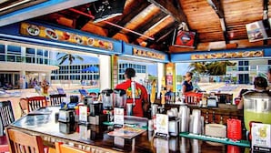 A restaurant with a wooden interior, a bar area, and large windows overlooking a beach.