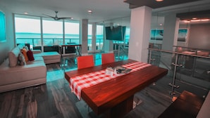 A modern living room with a dining area, large windows, a ceiling fan, and a TV. - Castle BTH2 Beach Townhouse, Pool and Direct Beach Access from the unit! Gym, Tennis, Free Valet (Miami Beach)