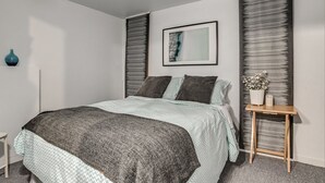 A modern bedroom with a bed, a bedside table with a vase, and a framed picture on the wall.
