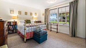 Une chambre à coucher comprenant un lit, des tables de chevet, une fenêtre avec des rideaux, une bibliothèque et un sol recouvert d’une moquette.