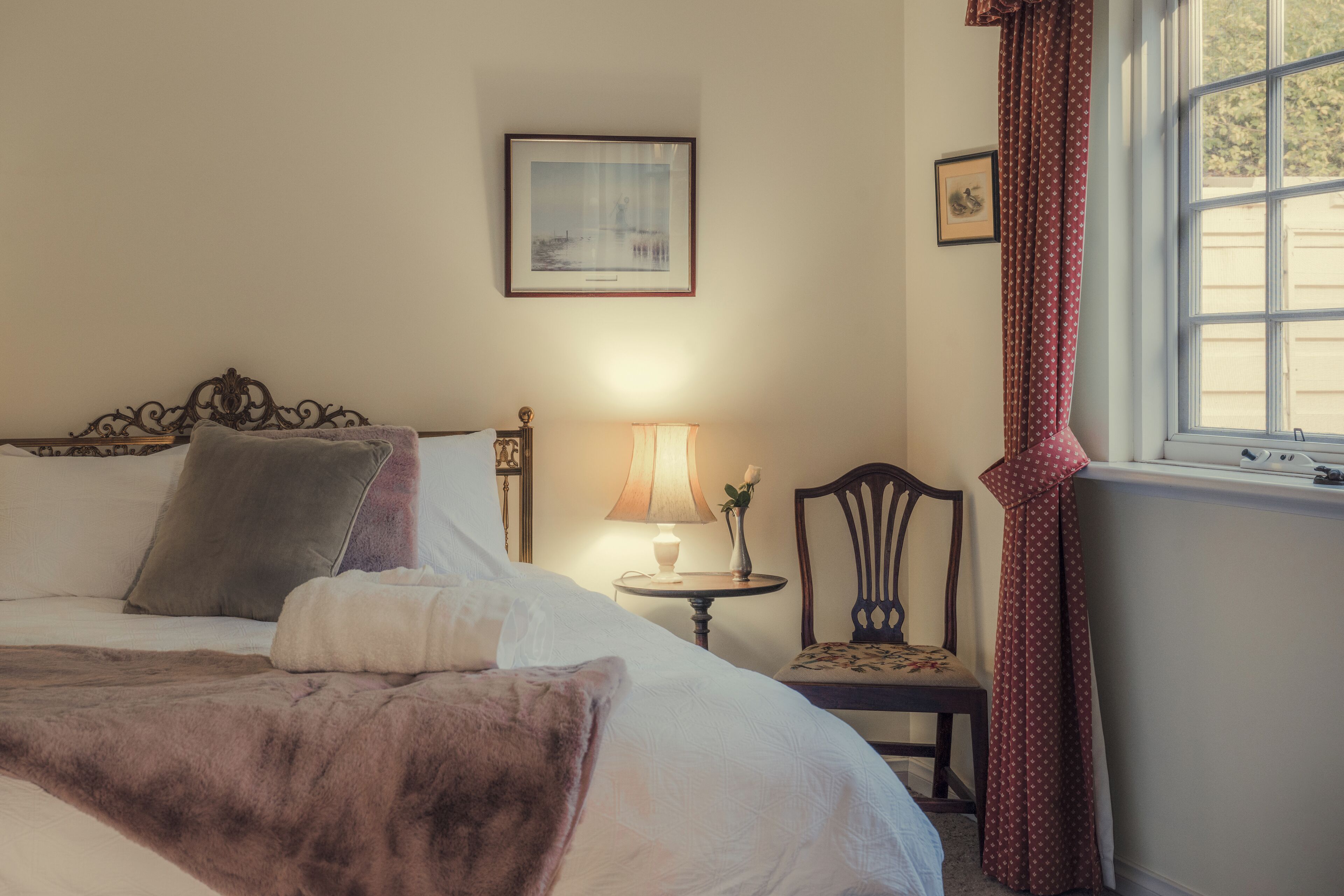 A neatly made bed with a brown throw blanket, a bedside lamp, and a framed picture on the wall.