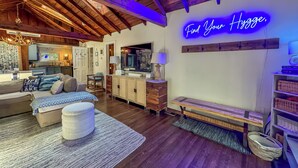 A cozy living room with a wooden ceiling, a neon sign reading "Find Your Hygge," and a television on a wooden stand. - Iconic Private DCL Lakefront Cabin + Hot Tub (Swanton)