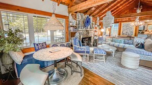 A cozy living room with a stone fireplace, wooden ceiling beams, and a mix of seating including a sofa, chairs, and a round table. - Iconic Private DCL Lakefront Cabin + Hot Tub (Swanton)