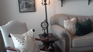Ein Wohnzimmer mit einem Holzschaukelstuhl, einem kleinen Tisch mit einer Lampe, einem Sofa und zwei gerahmten Bildern an der Wand.