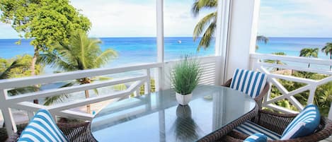 Ein Balkon mit Korbmöbeln, einem Glastisch und Blick auf das Meer.