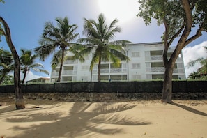 Ein Hotel direkt am Strand mit mehreren Balkonen, Palmen und einem Sandstrand.