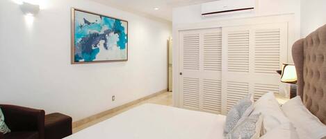 Quarto de hotel com uma cama, ventoinha no teto, ar condicionado, um quadro na parede e uma porta com persianas.