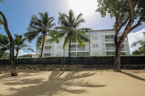 Un hôtel situé en bord de mer, doté de nombreux balcons, de palmiers et d’une plage de sable.