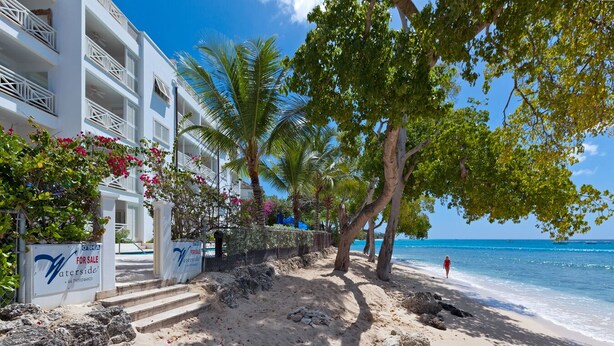 A beachfront hotel with a sandy walkway, palm trees, and a clear view of the ocean.