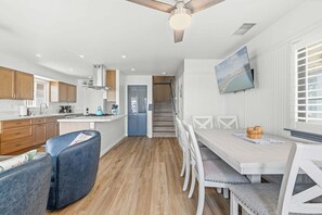 Une cuisine moderne avec des meubles en bois, un coin repas avec une table et des chaises blanches, et un escalier menant à un autre niveau.