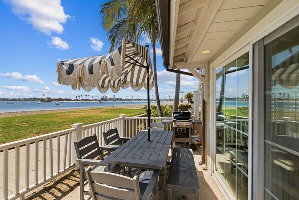 Une terrasse avec une table et des chaises, un barbecue et une vue sur la plage.