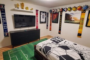 Un dormitorio con cama, televisor, cómoda y recuerdos deportivos en la pared.