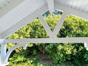 A white gazebo with a triangular roof structure, surrounded by lush green foliage.