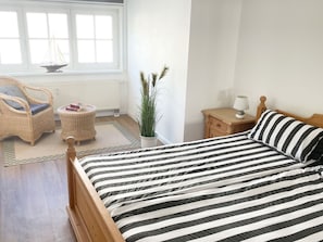 A bedroom with a bed, a chair, a nightstand, a lamp, a window, and a radiator.