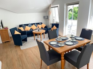 A modern living room with a sofa, chairs, a dining table set for four, and a view of the outdoors. - Villa Amanda - Strandnahe Fewo in Zentraler Aber Ruhiger Lage in Binz - Villa Amanda Fewo Nr.09 (Binz)