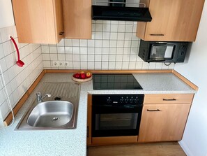 Una cocina compacta con lavamanos, estufa, microondas y armarios de madera.