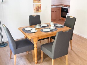 A dining table set for four with black chairs, a wooden table, and a kitchen in the background.