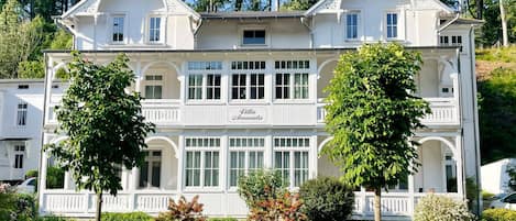 Un grand bâtiment blanc à deux étages, doté d’un balcon et d’une enseigne sur laquelle on peut lire « Villa Amanda ».