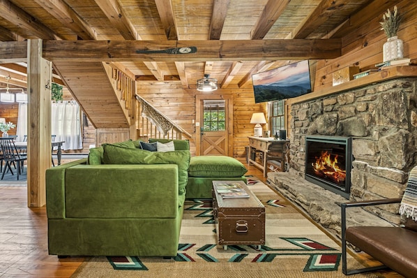Una sala de estar acogedora con chimenea de piedra, sofás verdes y techo de madera.