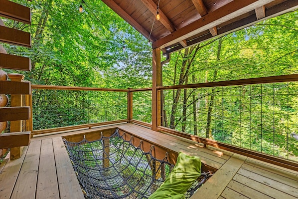 Eine Holzterrasse mit einer Hängematte und Blick auf einen dichten Wald.