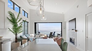 A modern kitchen with a large island, a dining area with chairs, a fireplace, and a view of the ocean.