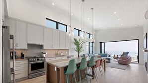 A modern kitchen with a central island, bar stools, and a view of the ocean.