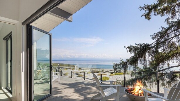 Un balcon avec un foyer extérieur, des chaises blanches et une vue sur la plage et l’océan.