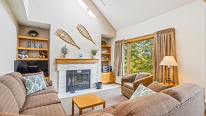 A cozy living room with a fireplace, sofas, a coffee table, and a bookshelf with decorative items. - Welcoming Two condo with pool, hot tub, and more- J3 (Killington)