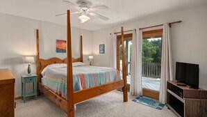 Ein Schlafzimmer mit einem Himmelbett, einem Deckenventilator, einem Fernsehschrank und einem Fenster mit Vorhängen.