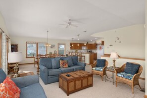 A spacious living room with a sofa, chairs, and a coffee table. There is a dining area with a table and chairs, and a kitchen in the background. - Sunshine Daydream - Oceanside, Private Pool, Hot Tub and Game Room (Corolla)