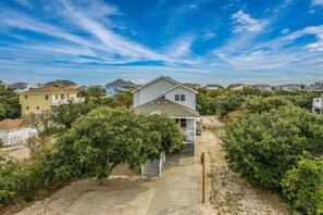 A residential area with houses, a clear sky, and a pathway leading to a house with a porch. - Sunshine Daydream - Oceanside, Private Pool, Hot Tub and Game Room (Corolla)