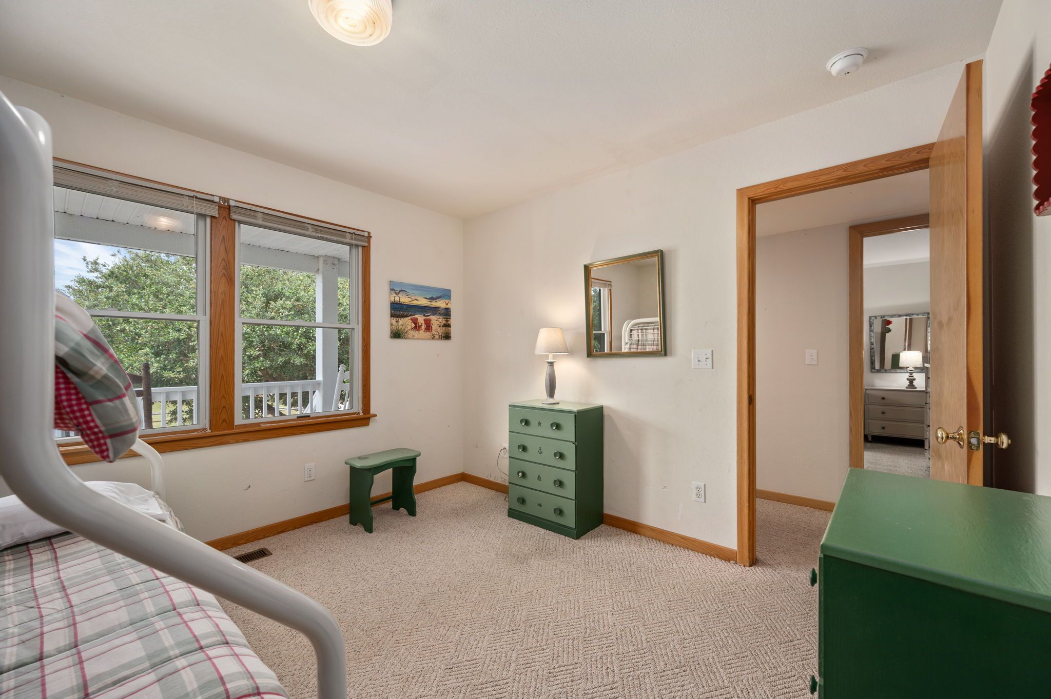 A bedroom with a bed, a dresser, a nightstand, a window, and a door leading to another room.