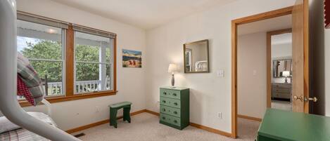 A bedroom with a bed, a dresser, a nightstand, a window, and a door leading to another room.