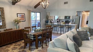 Un salón espacioso con un sofá grande de color gris, una zona de comedor con sillas de madera y un mantel a cuadros, y una cocina con electrodomésticos modernos.