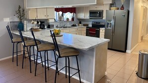 Una cocina moderna con una isla de mármol, taburetes de bar, electrodomésticos de acero inoxidable y vistas al exterior.