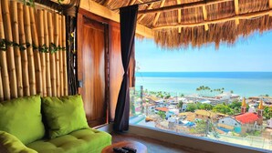 A room with a green sofa, a small wooden table, and a view of the sea and a town. - Tree-House Apt with Panoramic Ocean View+Pool+Steps to Beach & Malecon/Boardwalk (Puerto Vallarta)