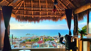 A room with a thatched roof, a view of the sea, and a balcony with a table and chairs. - Tree-House Apt with Panoramic Ocean View+Pool+Steps to Beach & Malecon/Boardwalk (Puerto Vallarta)