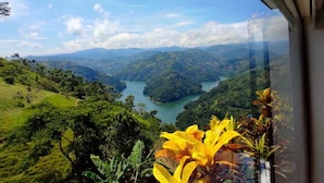 Vista da janela sobre um vale verdejante com rio, rodeado por vegetação e montanhas.