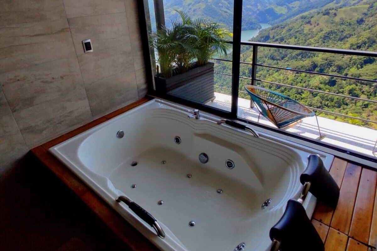 Een moderne badkamer met een groot bad, een houten vloer en uitzicht op een bergachtig landschap door een groot raam.